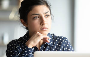 Woman sitting in front of laptop, thinking.